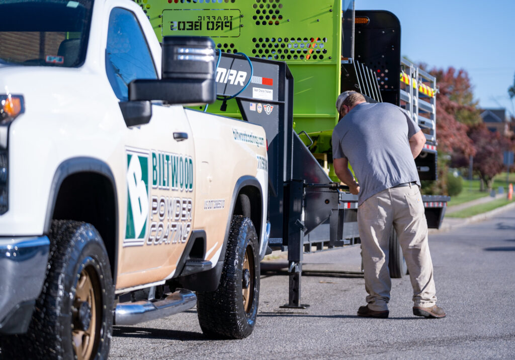 Biltwood Powder Coating truck with trailer being hitched by employee outside facility.