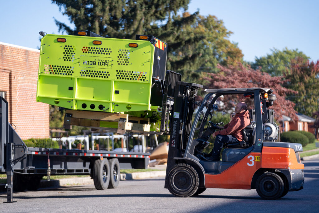 Forklift unloading bright green industrial equipment with powder-coated finish at Biltwood Powder Coating facility.