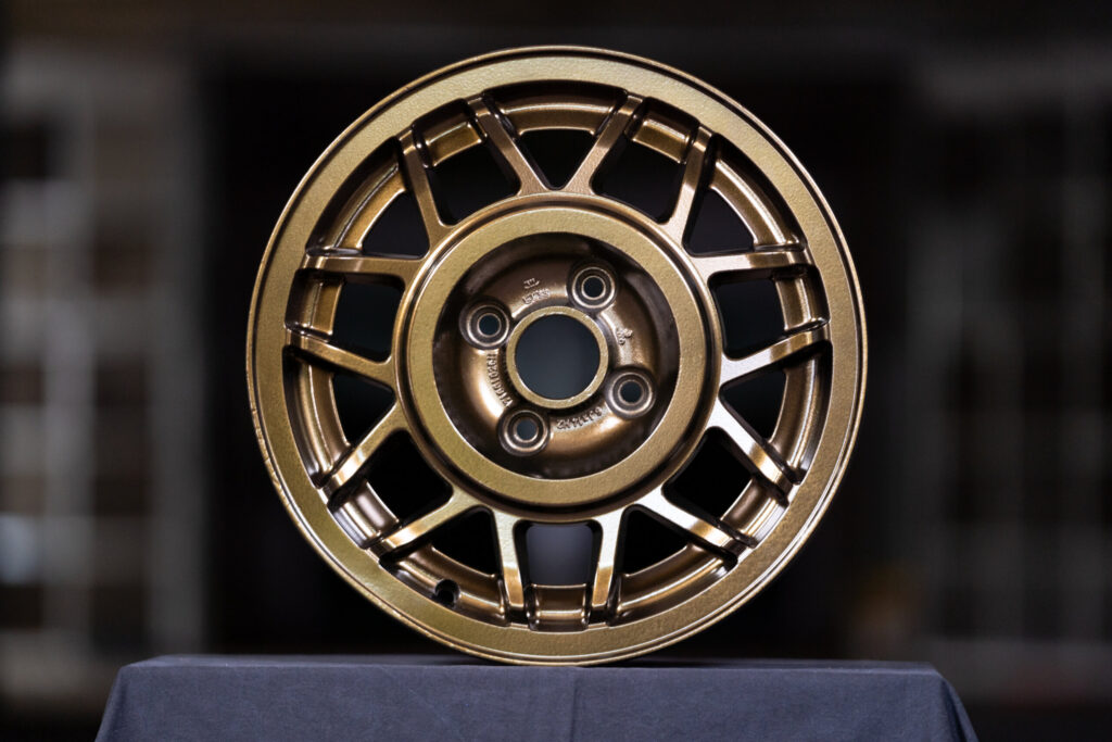 Bronze powder-coated multi-spoke wheel rim displayed on black fabric by Biltwood Powder Coating.